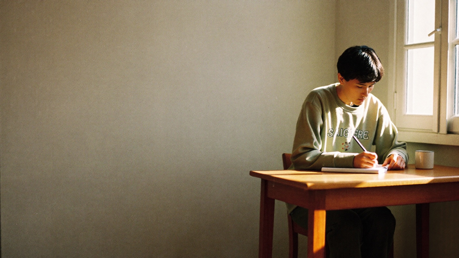 Person journaling at a sunlit wooden desk in the early morning